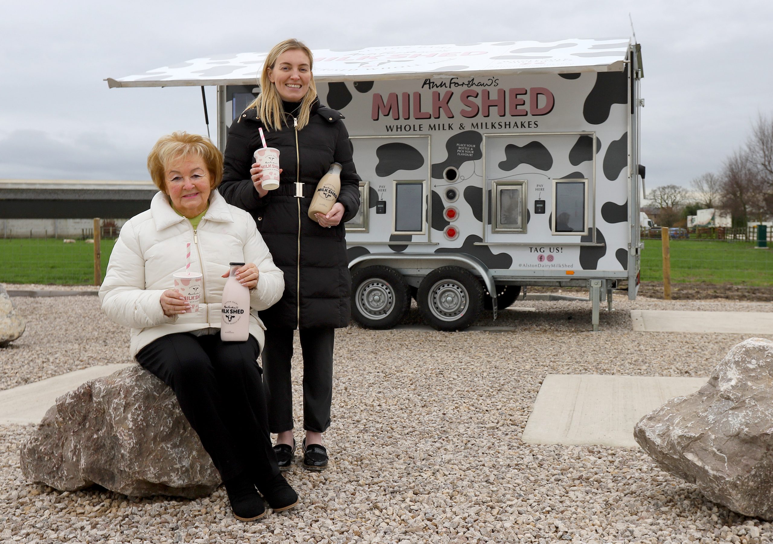 Alston Dairy Directors Ann Forshaw and her granddaughter Emma Baker holding a selection of the milkshakes with a backdrop of the Milk Shed.