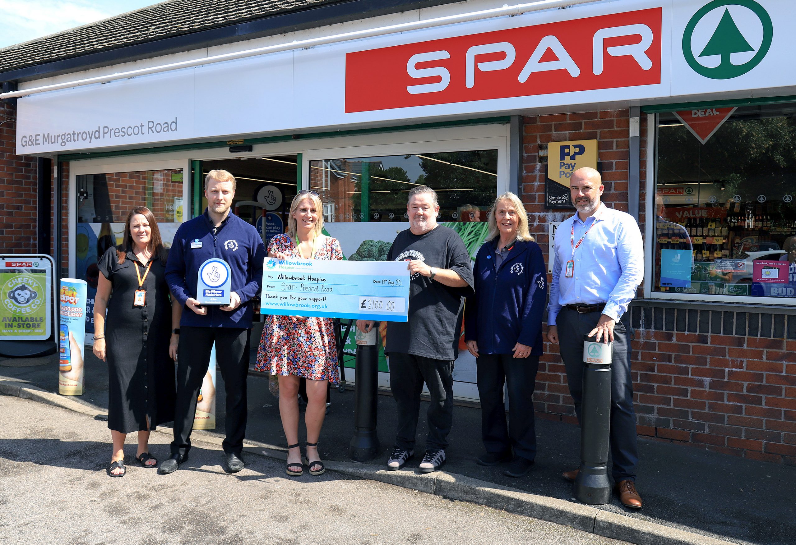 Members of the SPAR Prescot Road team in St Helens are joined by Bev Neilson and charity Patron Johnny Vegas for the £2,100 cheque presentation.